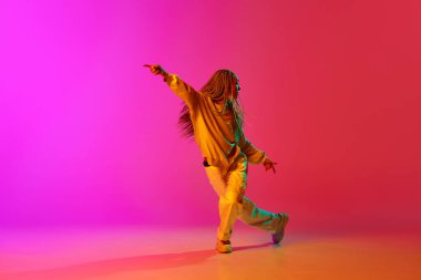 Hip-hop. Genç bir kızın portresi, saçı örgülü, tutkulu bir şekilde neon ışıkta pembe arka planda dans eden ilham verici bir dansçı. Çağdaş dans tarzı, hareket, sanat, hareket, reklam konsepti