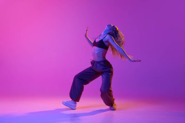 Serbest stil. Çekici bir genç kadın, atkuyruklu kız neon ışıklarıyla mor stüdyoda zevkle tek başına dans ediyor. Çağdaş dans, sanat, spor, moda, hobi kavramı