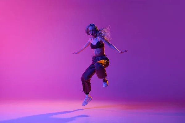 改善だ 1人のダンサー カジュアルな服を着ている女性がグラデーションの紫色のネオンの背景の上に動きにジャンプします コンテンポラリーダンスのスタイル インスピレーション ファッション アートの概念 — ストック写真