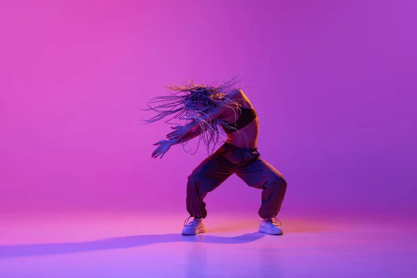 飛行編組ドレッド ネオンの光の中でグラデーションの紫色の背景に手で踊るピグテールを持つ1人の若い女の子 インスピレーションを受けたダンサーと肖像 コンテンポラリーダンスのスタイル アート 広告コンセプト — ストック写真