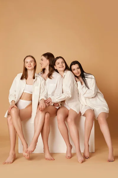 工作室拍摄与一群年轻漂亮的女孩 妇女白衬衫坐在米色的背景 自然美的概念 身体和皮肤护理 健康饮食 化妆品 — 图库照片