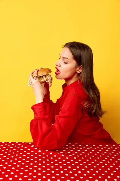 迷人而饥饿的女人在黄褐色的工作室背景下吃着渴望的大汉堡的肖像 废弃的流行艺术 明亮的色彩 美容美发 广告的概念 — 图库照片