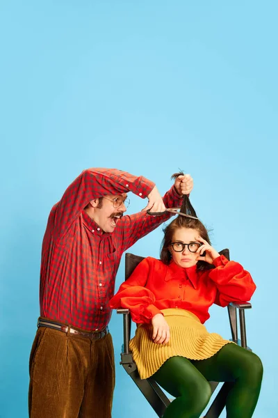 Bad service. Portrait with sad, upset woman, client and crazy barber, female hairdresser doing new haircut over blue background. Concept of barbershop, new style, beauty, fashion, human emotions, ad