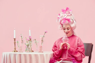 Peri kuyruklu genç prenses büyük pembe peruk takıyor ve pembe stüdyo arka planında heyecan verici bir yüzü olan şarap kadehini tutuyor. Devir, modernlik ve rönesans karşılaştırması, güzellik, tarih kavramı
