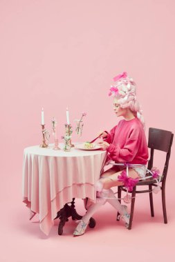 Kraliyet kahvaltısı. Zarif prenses portresi, pembe elbiseli kraliçe ve pembe stüdyo arka planında peruk yiyen. Devir, modernlik ve rönesans, güzellik ve tarih karşılaştırması kavramı