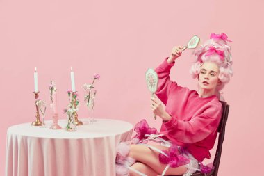 Güzellik salonu. Pembe elbiseli, el aynası tutan ve pembe arka planda saç stili yapan bir prenses portresi. Devir, modernlik ve rönesans, güzellik ve tarih karşılaştırması kavramı