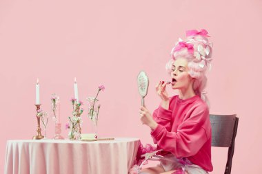 Güzellik salonu. Güzel prensesle portre, büyük peruk takan, el aynası tutan ve pembe arka planda ruj kullanan bir kraliçe. Devir, modernlik ve rönesans, güzellik ve tarih karşılaştırması kavramı