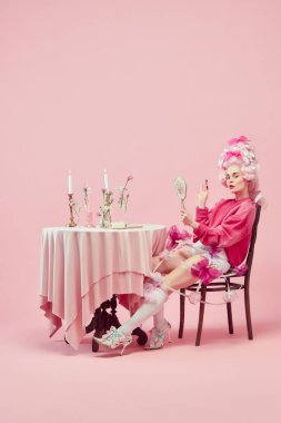 Partiye gidiyorum. Güzel prensesle portre, büyük peruk takan kraliçe pembe arka planda ruj sürerek makyaj yapıyor. Devir, modernlik ve rönesans, güzellik ve tarih karşılaştırması kavramı