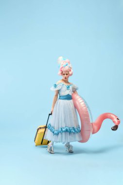 Genç prensesle portre, elinde bavul taşıyan kraliçe ve şişme flamingo mavi arka planda seyahat edecek. Devir, tatil, yaz, hafta sonu, rahatlama karşılaştırması kavramı