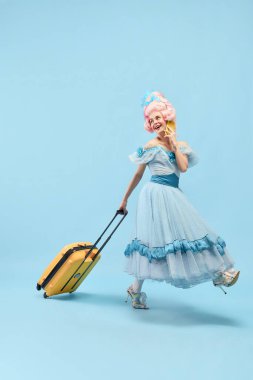 Mutlu genç prenses portresi, büyük pembe peruklu kraliçe elinde bavulla mavi arka planda cep telefonuyla konuşuyor. Seyahat kavramı, dönem karşılaştırması, tatil, yaz, hafta sonu, duygu