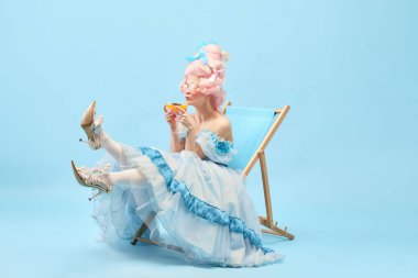 Uzun zamandır beklenen bir tatil. Genç prensesin portresi, zarif bir elbise giymiş güneş yatağında oturmuş mavi arka planda kokteyl içen bir kraliçe. Dönem karşılaştırması kavramı, rahatlatıcı, parti, yaz, reklam