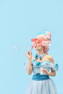 Prenses portresi, baloncuklarla oynayan elbise giyen ve mavi stüdyo arka planında gülümseyen bir kraliçe. Devir, modernlik, barok stil, güzellik, moda, insani duyguların karşılaştırılması kavramı