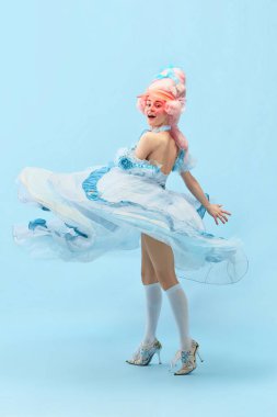 Şık ve neşeli. Prenses portresi, Kraliçe elbisesiyle daireler çiziyor ve mavi stüdyo arka planında gülümsüyor. Devir, modernlik, barok stil, güzellik, moda, duygu karşılaştırması kavramı