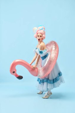 Komik güzel prensesin portresi, üzerinde pembe şişme flamingo taşıyan bir kraliçe ve mavi arka planda plaja gidiyor. Devir, tatil, yaz, hafta sonu, rahatlama karşılaştırması kavramı