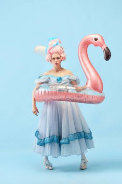 Komik, üzgün prenses, güzel elbiseler giyen kraliçe pembe şişirilebilir flamingo tutuyor ve mavi arka planda yüzüyor. Devir, tatil, yaz, hafta sonu karşılaştırması kavramı