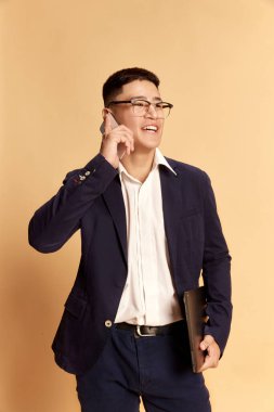 Moda tarzı kostüm giymiş, takım elbiseli, bej arka planda yalnız poz veren çekici bir genç, öğrenci ya da ofis memuruyla portre. İş, öğrenim, insan duyguları, moda, çevrimiçi, satış kavramı