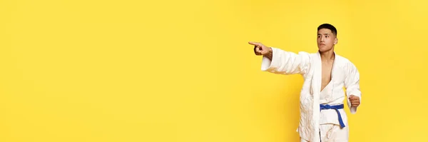 横幅与年轻人 跆拳道 空手道运动员身穿白色和服准备一场决斗黄色工作室背景 健康生活方式的概念 — 图库照片