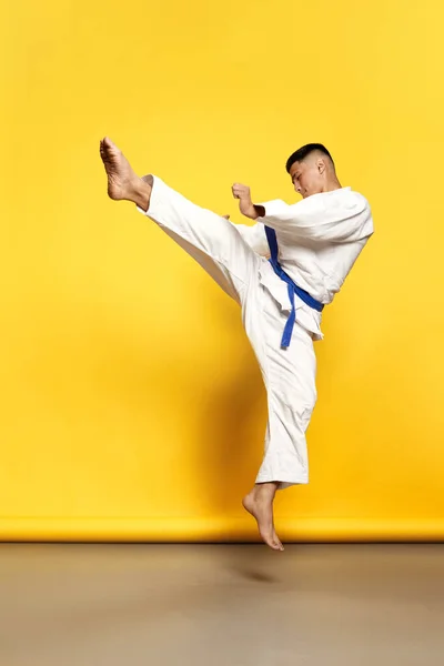 黄色の背景の上に基本的な動きを行う白い着物を着てプロの男性Taekwondo 空手選手の肖像画 スポーツ スキル 健康的なライフスタイルの概念 — ストック写真