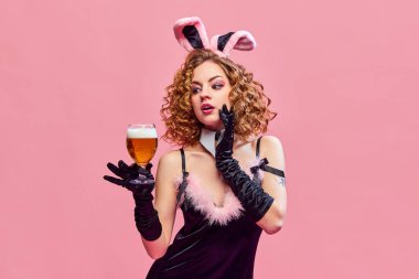 Genç ve güzel bir kızın portresi. Tavşan kostümü giymiş, kulakları pembe arka planda bir bardak bira tutan bir kadın. İçki, alkol, Ekim Festivali, festivaller, dinlenme, tatil, parti, reklam
