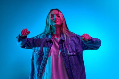 Sorunlarla uğraşmak. Mavi stüdyo arka planında pembe neon ışıkta yumruklarını gösteren genç ve sevimli bir kızın portresi. Meydan okumalar, insani duygular, güç, dövüş sanatları, reklam