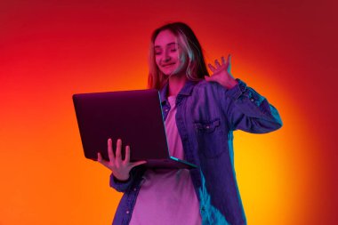 Online eğitim. Bir genç kız, kulaklık takan ve elinde dizüstü bilgisayarla ekranda kırmızı arka planda gülümseyen bir öğrenci. Duyguların kavramı, öğrenci hayatı, gençlik, öğrenim, reklam