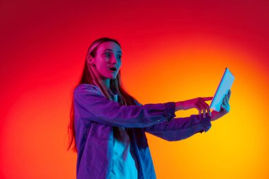 Sürpriz, heyecan verici. Tablet tutan, ağzı açık ve heyecanlı bir yüz ifadesiyle bakan sıradan kıyafetler giyen sevimli bir kız. İnsan duyguları kavramı, ruh hali, cihazlar, müzik, sohbet, reklam