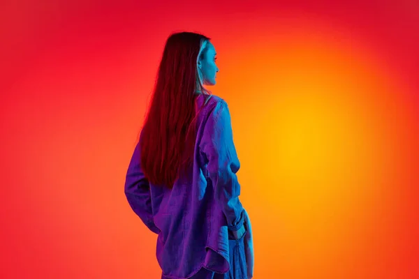 Pensive person. Back view portrait with sad, upset woman, girl with long hair posing over red background in neon light. Concept of beauty, youth, human emotions, fashion, temporary difficulties, ad