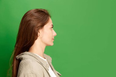 Yeşil renkli stüdyo arka planında sakince poz veren büyük gözlü genç, güzel ve pozitif bir kızın yan görüntüsü. Güzellik kavramı, gençlik, insan duyguları, moda, kozmetoloji, reklam