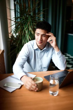 Modern şehir kafesinde çalışan, klasik kıyafetler giyen, laptoplu ve masa başında kağıtları olan genç dalgın bir iş adamı. Serbest iş, iş adamları, uzak iş, kariyer büyümesi, reklam kavramı