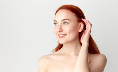 Güzel bir mankenle portre, çıplak omuzlu ve beyaz stüdyo arka planında gülümseyen kızıl saçlı bir kız. Saç bakımı, kozmetik, kozmetik, reklam, doğal güzellik, spa