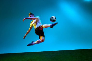 Bir sporcu, sarı ve siyah üniformalı bir futbolcu neon ışıkta futbol sahasında topa vuruyor. Eylem konsepti, enerji, spor, takım oyunu, şampiyonluk, rekabet, reklam