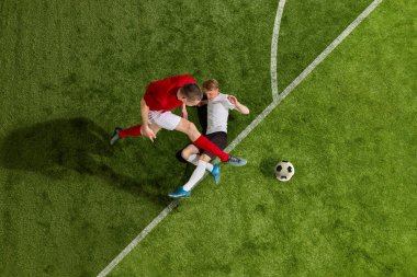Futbol oyuncularının spor üniformalı ve yeşil çimen arka planında top için mücadele eden futbol botlarının hava görüntüsü. Profesyonel spor, takım, yarışma, şampiyonluk kavramı