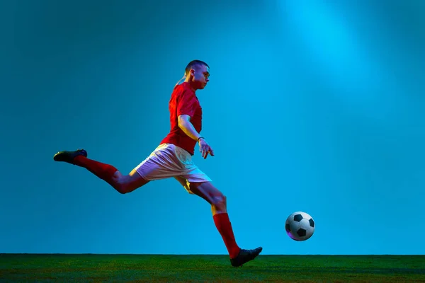 体育赌博 足球的动态肖像 身穿运动服的足球运动员把球踢过场地 体育场背景在霓虹灯下 团队游戏 锦标赛 广告的概念 — 图库照片