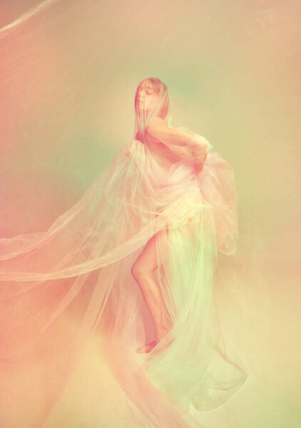 Young pretty woman with perfect body shape posing with covered transparent fabric over pastel color palette background. Natural beauty of female body concept. Highlights glow effect