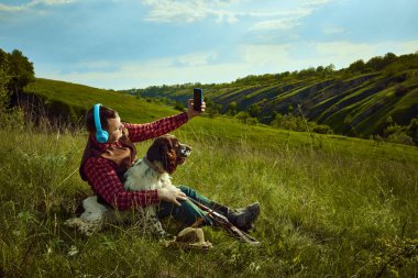 Erkek partisi. Kulaklık takan bir adamın portresi köpeği İngiliz spanyel ile çimenlerde oturuyor ve doğa manzarasında avlandıktan sonra dinleniyor. Av kavramı, hobi, ad