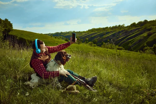 stock image Mens party. Portrait with man wearing headphones sitting on grass with his dog English springer spaniel and resting after hunting on nature landscape background. Concept of prey, hobby, ad