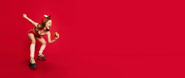 美しい女性 赤い髪を持つローラーの上のウェイトレスは大きなハンバーガーをポーズし 赤いスタジオの背景に笑みを浮かべています コピースペースのバナー 食べ物 人間の感情 広告の概念 — ストック写真