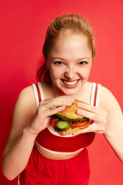 美丽的饥饿的女人 女孩抱着和吃着一个多汁的汉堡包渴望超过红色工作室的背景 可用于食品广告 靠近点食物 广告的概念 — 图库照片