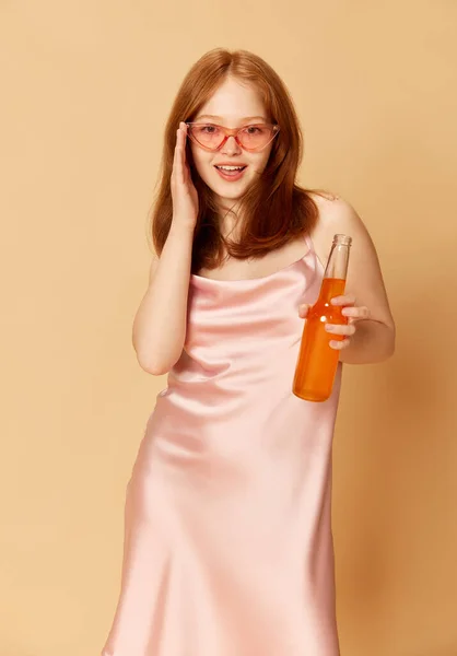 若いティーンエイジャーの肖像画 エレガントなピンクのドレスを着てドリンクボトルを保持し オレンジの背景に幸せな笑顔でカメラを見ている女の子 パーティー お祝い 広告の概念 — ストック写真