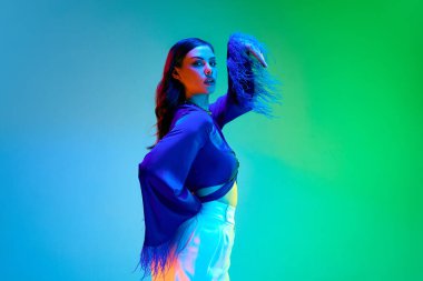 Parlak makyajlı güzel esmer kız mavi ipek bluz giyiyor ve neon arkaplan üzerinde tüyler var. Cazip bir ev elbisesi, lüks bir pijama. Güzellik kavramı, moda haftası, reklam