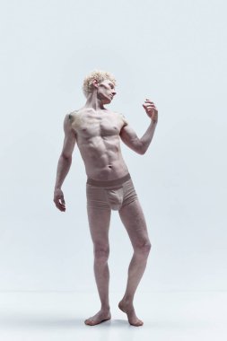 Beyaz stüdyo arka planında eski bir heykel gibi poz veren kıvırcık sarı saçlı üstsüz kaslı adamın portresi. Erkek vücudu estetiği, erkek güzelliği, ilham, sanat kavramı