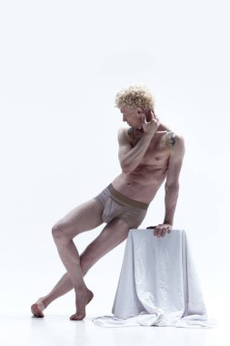 Beyaz arka planda izole edilmiş heykel gibi üstsüz poz veren, kıvırcık saçlı yakışıklı sarışın bir adam. Erkek antika heykeli. Erkek vücudu estetiği, erkek güzelliği, ilham, sanat, reklam kavramı