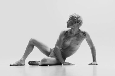 Beyaz stüdyo arka planında izole edilmiş heykel gibi üstsüz poz veren, iç çamaşırı giyen antika bir adamın portresi. Tek renkli olsun. Erkek vücudu estetiği, erkek güzelliği, sanat, reklam anlayışı.