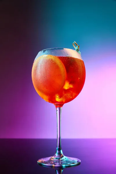 用Aperol Spritz的玻璃杯在渐变霓虹灯背景上的生动的肖像 酒精饮料的基础上普罗塞科 冰块和橙子 混合光 庆祝的概念 — 图库照片