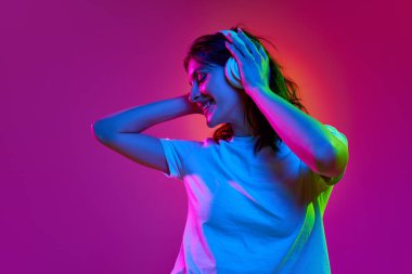 Mutlu, güzel bir genç kızın yakın portresi, kulaklıklı bir genç, müzikten hoşlanıyor ve neon ışıkta pembe arka planda gülümsüyor. Güzellik kavramı, gençlik, insani duygular, rüyalar, hobi, reklam