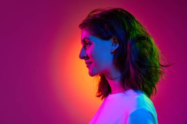 Neşeli bir ruh hali. Genç ve çekici bir kızın portresi, dalgalı saçlı bir öğrenci pembe stüdyo arka planında neon ışıklarıyla poz veriyor. Yan görüş. Güzellik kavramı, gençlik, insan duyguları, moda, kozmetoloji, reklam