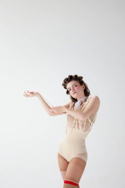 Kadınlık sanatı. Gri stüdyo arka planına karşı retro iç çamaşırlarıyla duran pembe yanaklı güzel, hassas genç bir kız. Kadın güzelliği, sanat, moda, duygu kavramı. Pin yukarı biçimi