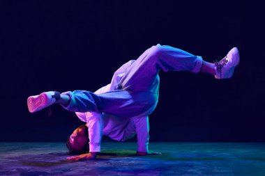 Spor tarzında giyinen aktif genç adamın hareketli görüntüsü neon ışıkta siyah stüdyonun arka planında breakdance yapıyor. Sokak dansı konsepti, moda, gençlik, hobi, dinamik, reklam