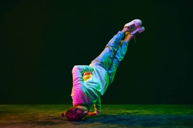 Dehşet saçan, spor kıyafetli, break dans yapan, hip-hop 'la neon ışıklı siyahi stüdyo arka planına karşı olan genç adam. Sokak dansı konsepti, moda, gençlik, hobi, dinamik, reklam