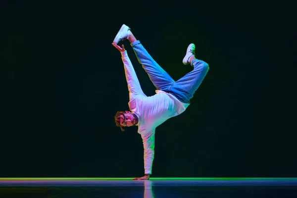 stock image Dynamic image of talented, active young man in sport style clothes dancing breakdance against black studio background in neon light. Concept of street style dance, fashion, youth, hobby, dynamics, ad